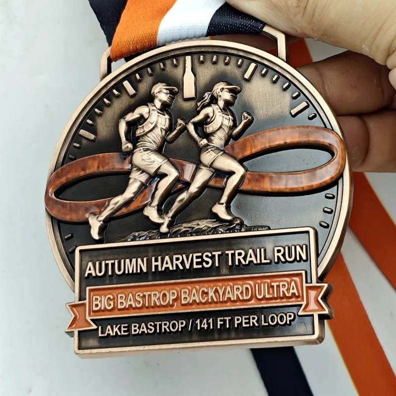 Finisher medal for the Big Bastrop Backyard Ultra at the Autumn Harvest Trail Run, showing two trail runners over an infinity loop