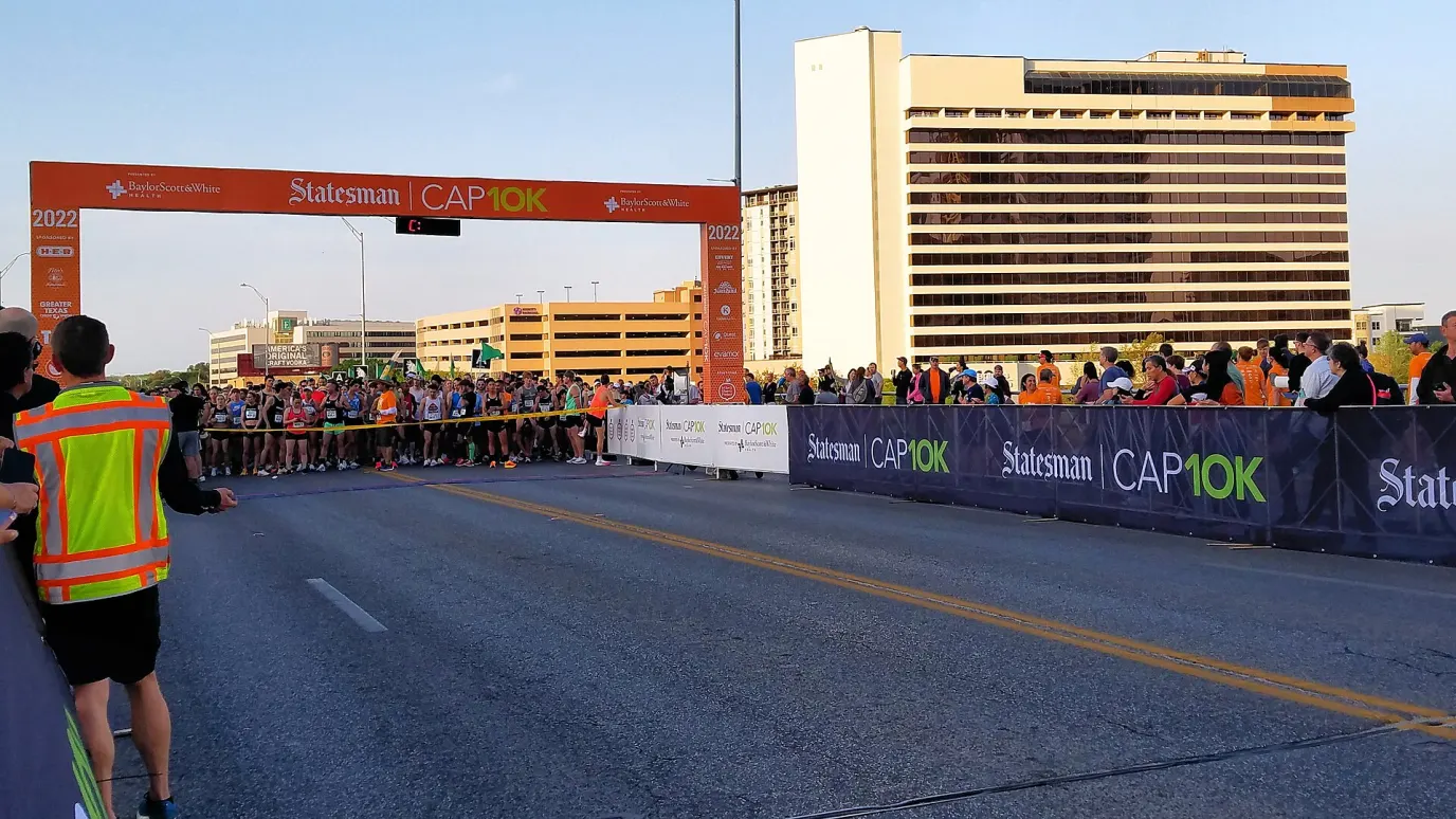 Runners lined up under the orange Cap10K start arch on a downtown Austin street at the 2022 race