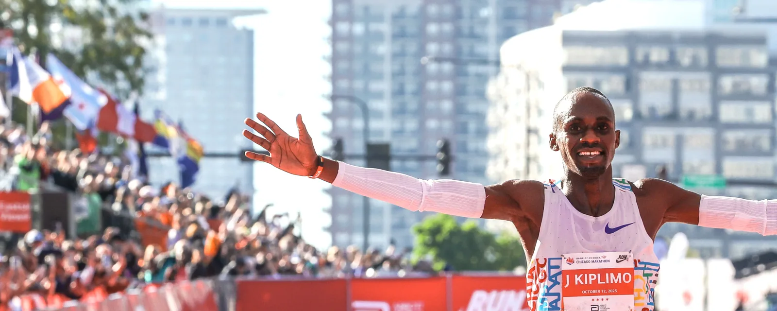 Jacob Kiplimo with arms spread wide as he wins the 2025 Chicago Marathon, crowds and flags behind him