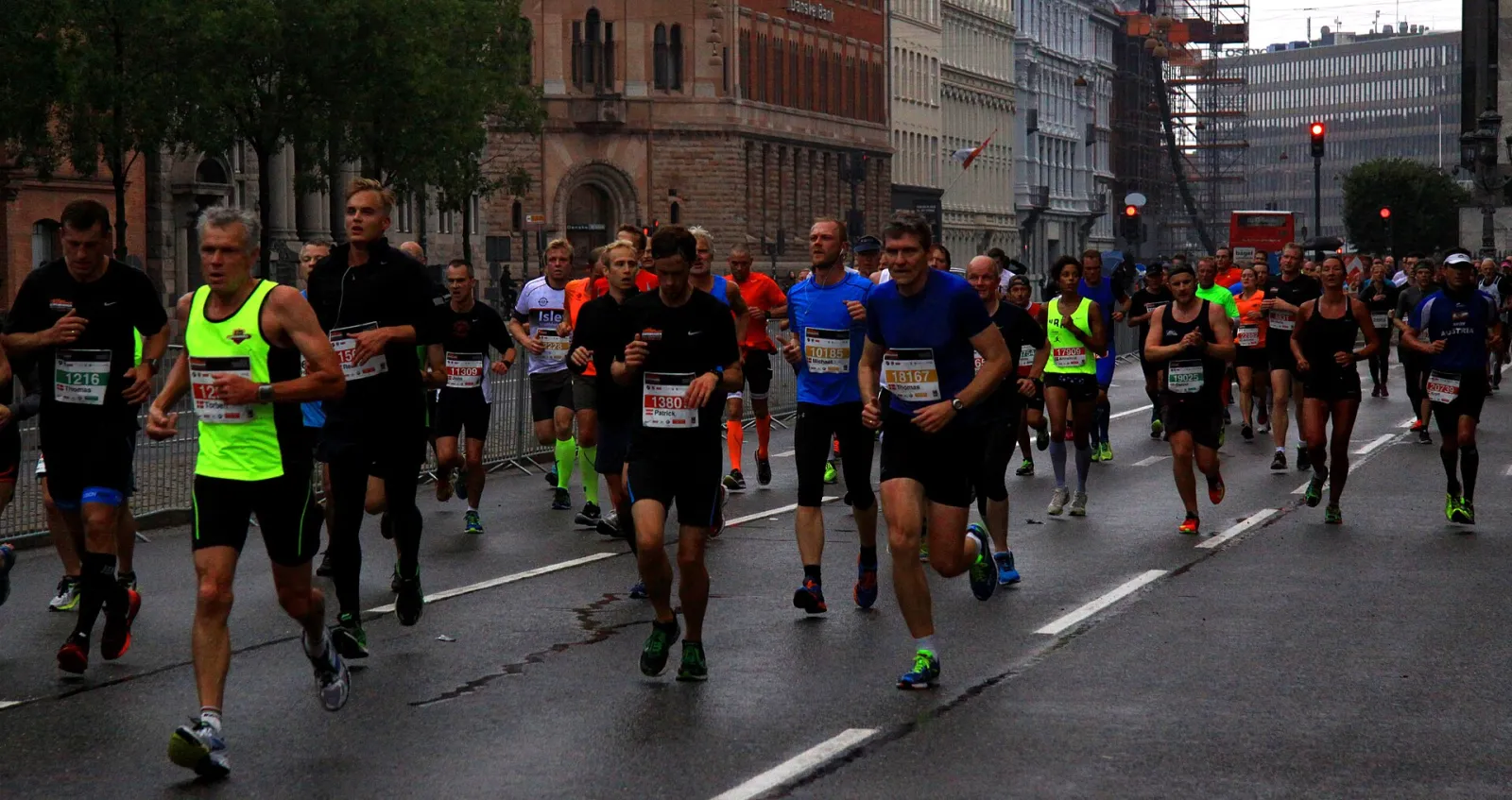 A pack of runners in bibs on a wet Copenhagen street lined with older buildings during the 2015 Copenhagen Half Marathon