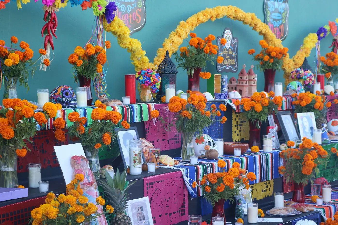 A tiered Día de los Muertos ofrenda covered in orange marigolds, candles, papel picado, sugar skulls and framed photos