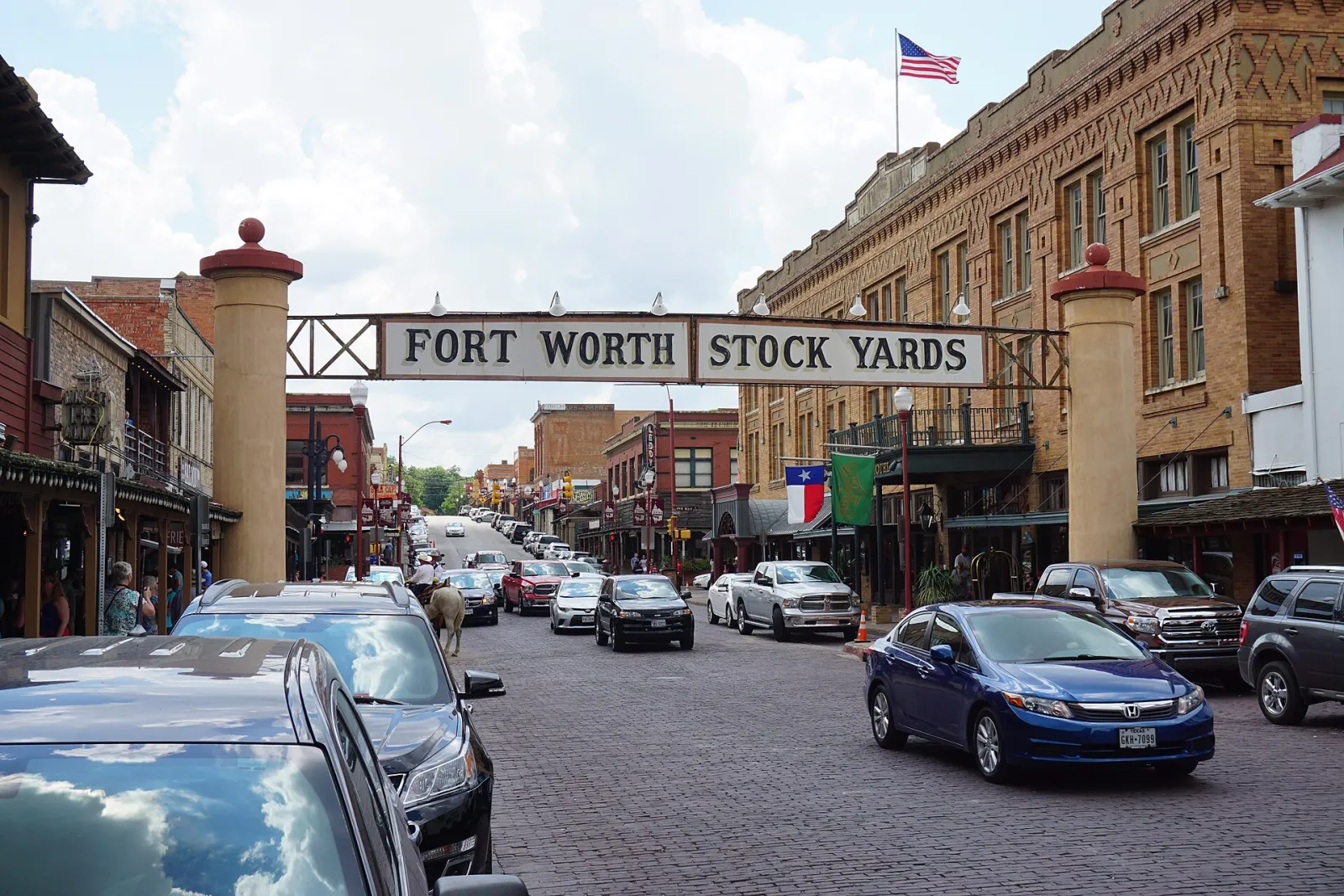 The Fort Worth Stock Yards arch over the brick pavement of Exchange Avenue, lined with historic buildings and parked cars