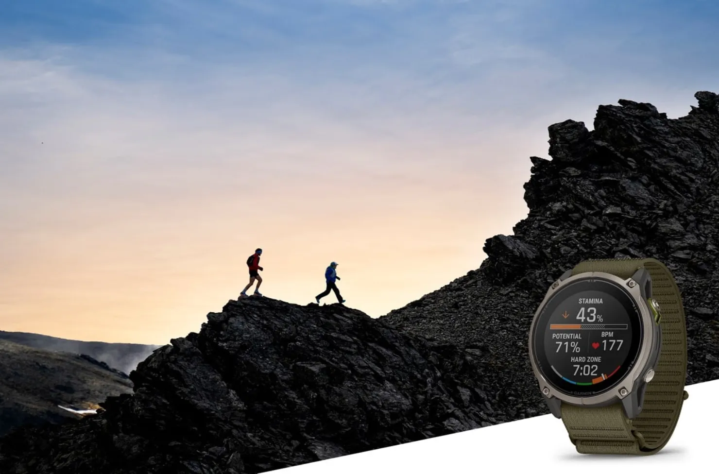 Two trail runners silhouetted on a rocky ridge at dusk beside a Garmin Enduro 4 with an olive fabric band showing stamina data