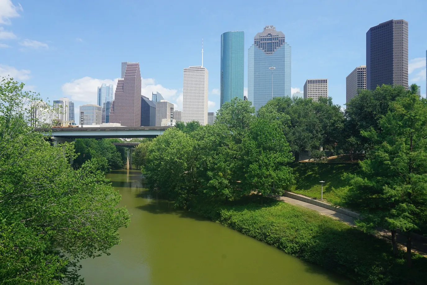 The downtown Houston skyline above Buffalo Bayou and the tree-lined trail in Buffalo Bayou Park
