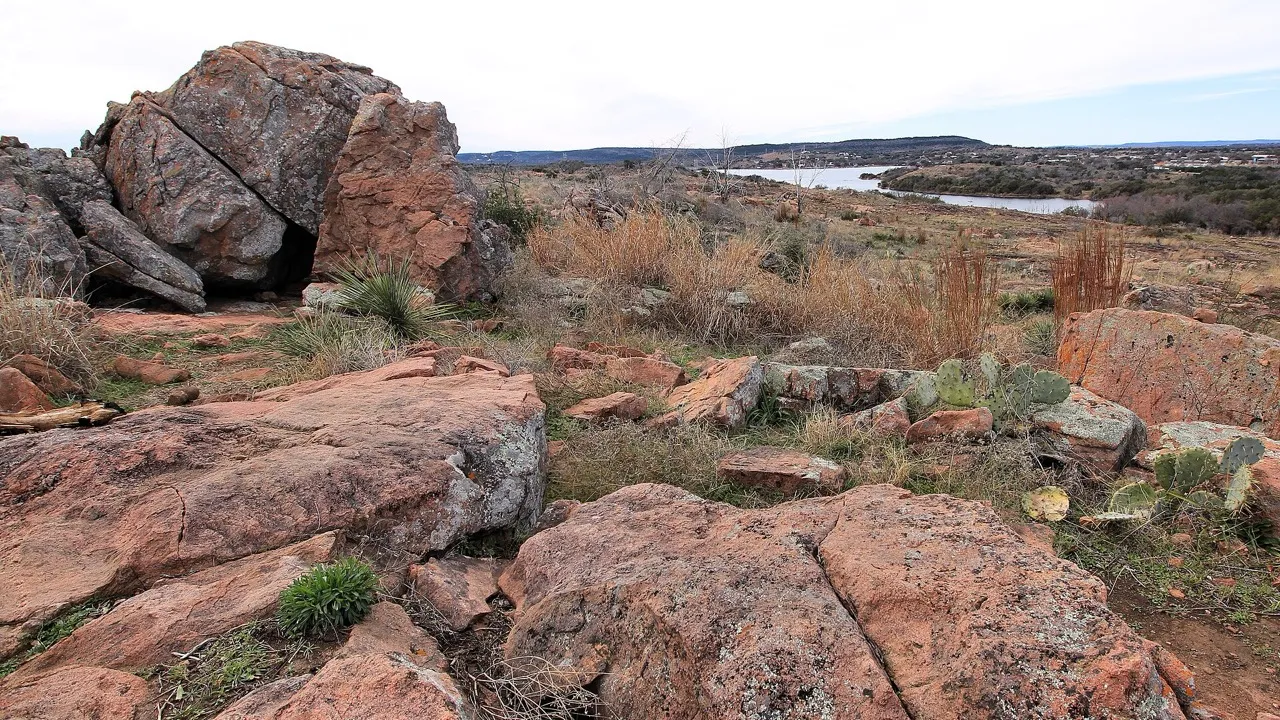 Pink granite boulders and dry grass on a hilltop overlooking Inks Lake in the Texas Hill Country