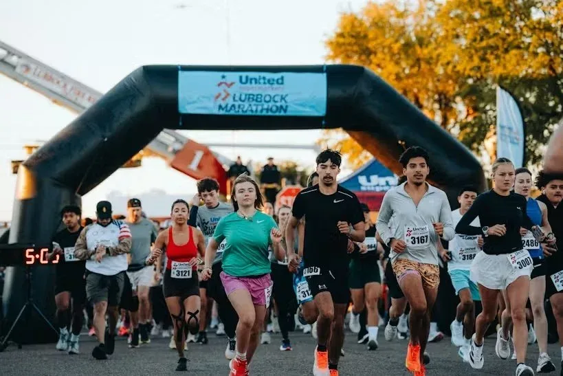 Runners surge under the United Supermarkets Lubbock Marathon inflatable arch at the start line