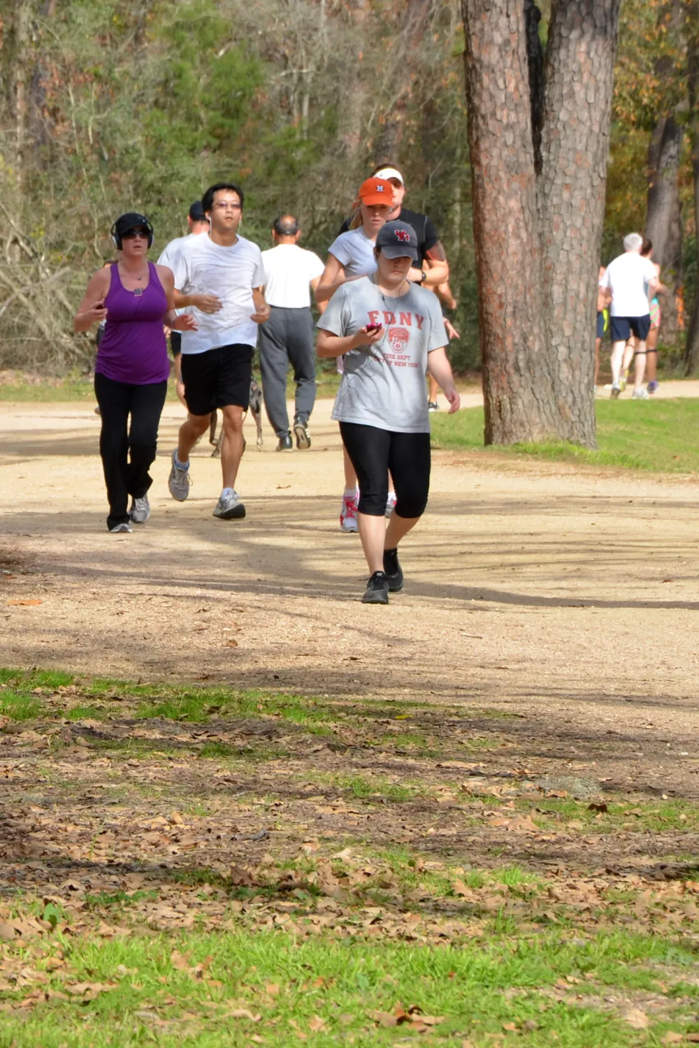Runners and walkers on the wide crushed-granite Seymour Lieberman trail under tall pines in Memorial Park, Houston