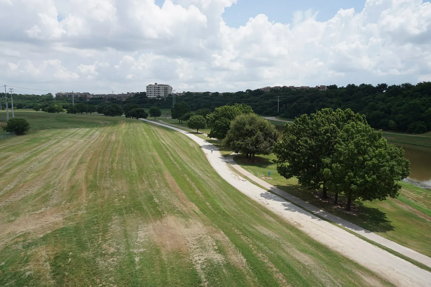 A wide gravel Trinity Trails path running along a grassy levee beside the Trinity River in Fort Worth, under summer clouds